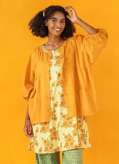 A woman wearing a yellow blouse and a floral jersey dress from Gudrun Sjödén.