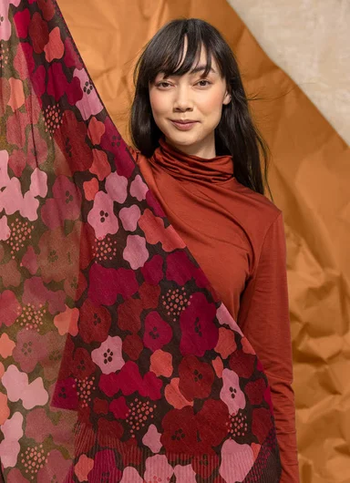 A woman holding up a patterned scarf from Gudrun Sjödén.