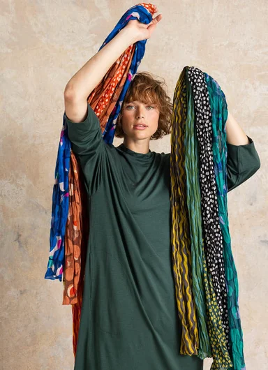 A woman holding a bunch of patterned and colourful scarves from Gudrun Sjödén in each hand.