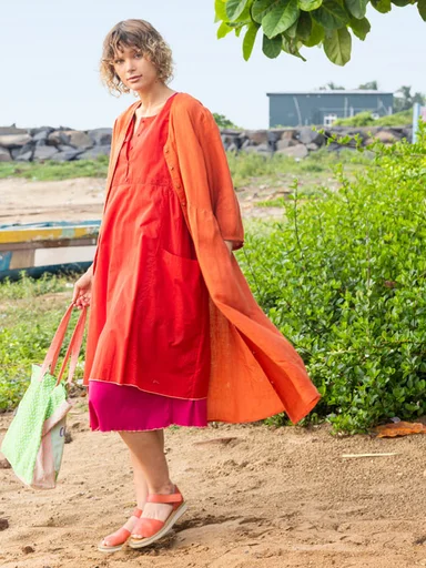 A woman on a beach wearing layers of orange clothes from Gudrun Sjödén.