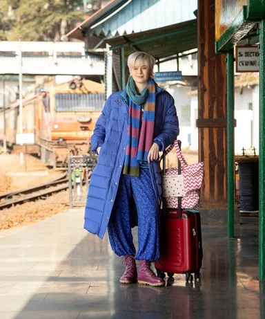 A woman walking along a railway station platform wearing layers of clothes from Gudrun Sjödén.
