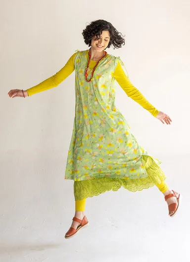 A jumping woman wearing layers of green and yellow clothes from Gudrun Sjödén.