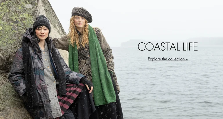 Two women posing by a rock face next to water, wearing clothes and accessories from Gudrun Sjödén’s 2025 Winter collection.