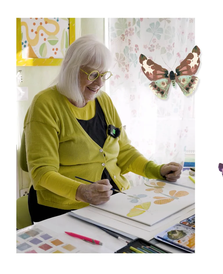 Gudrun Sjödén sitting at a desk painting watercolour butterflies. The picture also includes a standout image of a watercolour butterfly.