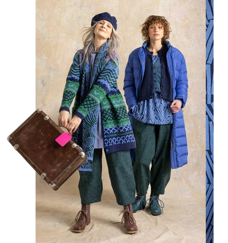 Two women holding travel luggage, wearing layered outfits from Gudrun Sjödén.