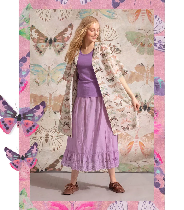 A woman against a butterfly background wearing a beige dress with a butterfly pattern from Gudrun Sjödén. The image also includes standout watercolour butterflies.
