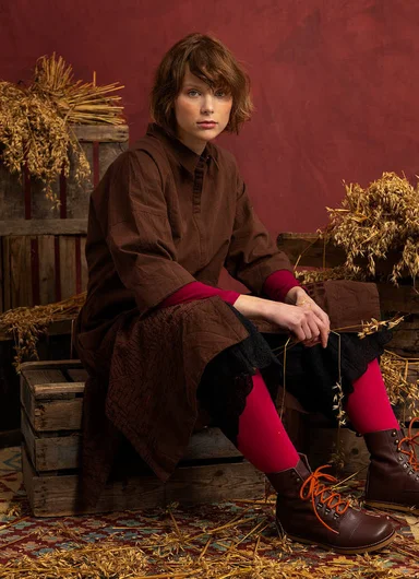 A seated woman wearing layers of clothes in low-key shades from Gudrun Sjödén.