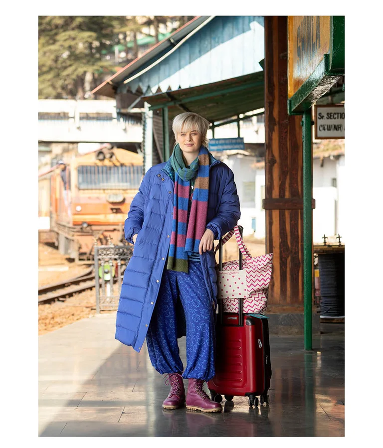 A woman wearing a long, blue down jacket and a striped knitted scarf from Gudrun Sjödén.