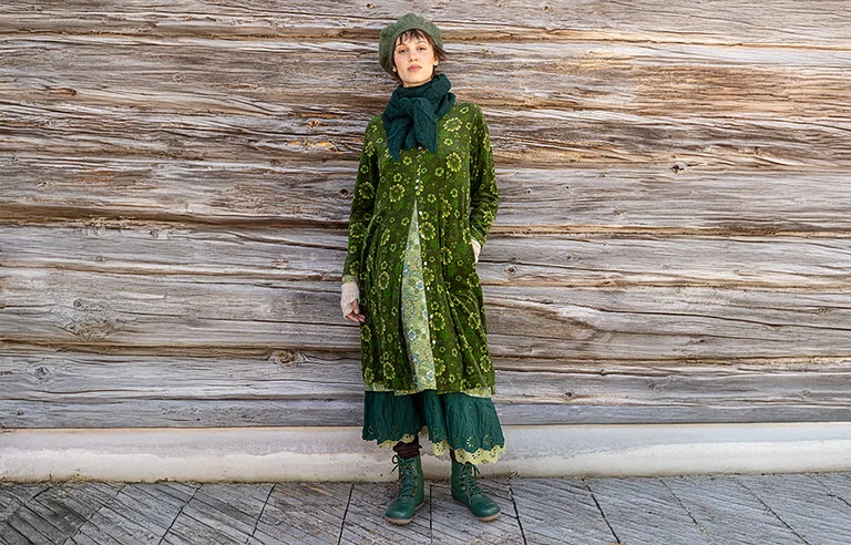 A woman in an animal mask walking in a snowy landscape wearing a knit beige and gray patterned sweater from Gudrun Sjödén’s holiday collection 2025. The picture also has a graphic-style red heart.