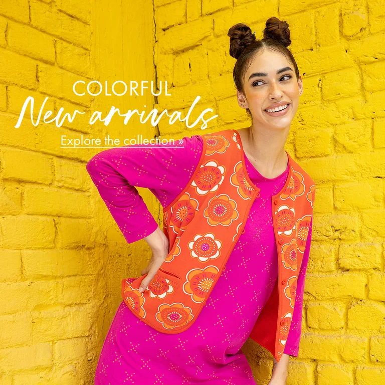 Two women posing in front of a yellow brick wall, wearing colorful clothing from Gudrun Sjödén.