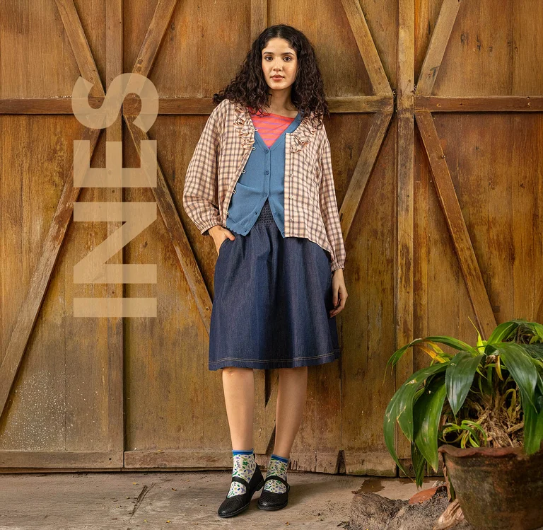 A woman leaning against a wooden wall wearing layers of clothes from Gudrun Sjödén.