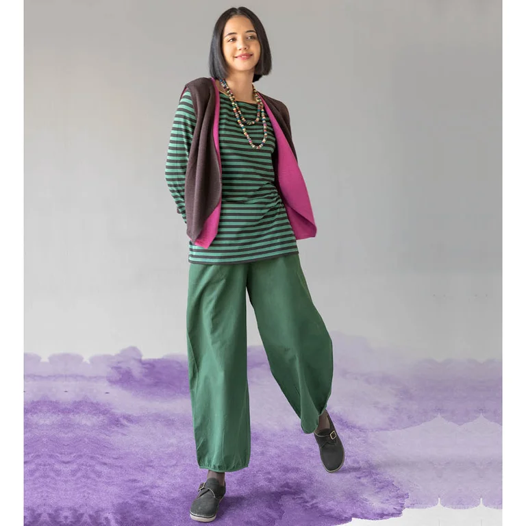 A woman wearing a green and dark blue striped top, a knitted waistcoat and green trousers from Gudrun Sjödén.
