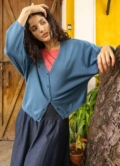 A woman leaning against a tree wearing a blue cardigan from Gudrun Sjödén.