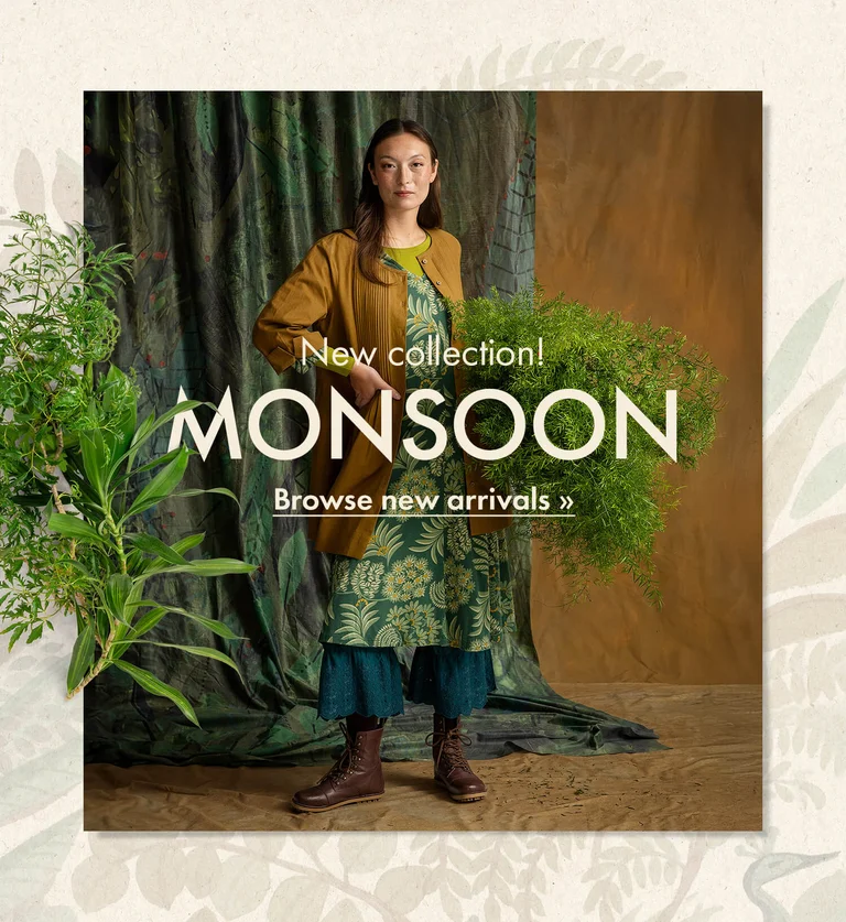 A woman with her hands in the air wearing a knitted cardigan in shades of blue from Gudrun Sjödén. The picture is framed by a botanical pattern and standout green plants.