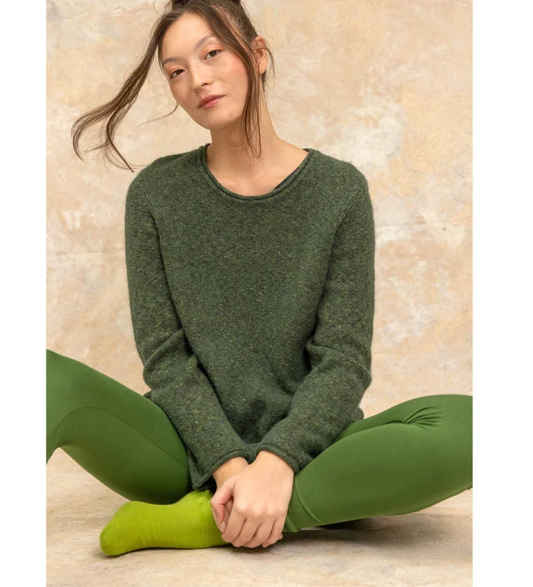 A seated woman wearing clothes in shades of green from Gudrun Sjödén’s Essentials range.