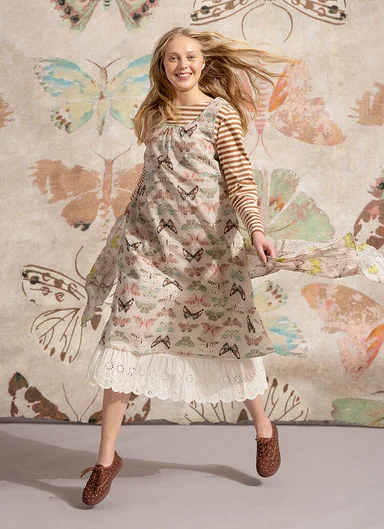 A woman against a butterfly background wearing a beige dress with a butterfly pattern from Gudrun Sjödén.