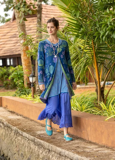 A woman holding a large, green leaf wearing layers of orange clothes from Gudrun Sjödén.