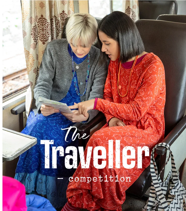Two women on a train, leaning over a map, wearing layers of clothes from Gudrun Sjödén.