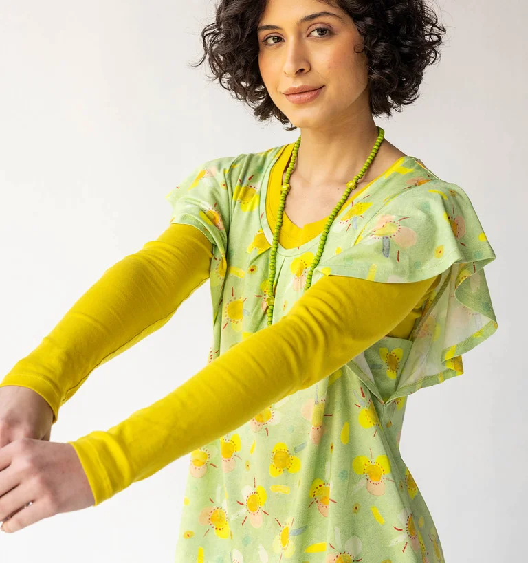 A woman dressed in a patterned green jersey-fabric top, worn over a yellow long-sleeved top from Gudrun Sjödén.