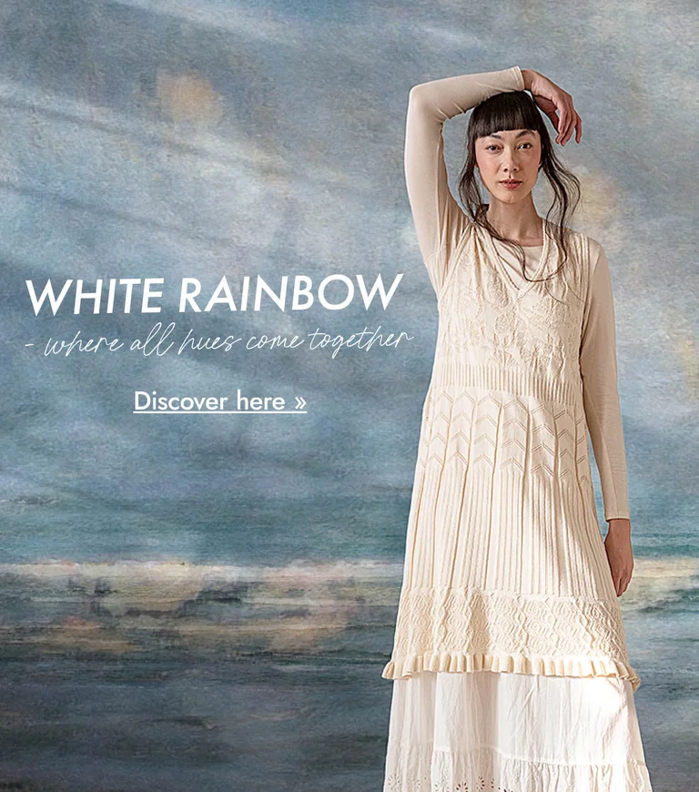 A woman wearing layers of white clothes from Gudrun Sjödén against a background that looks like an abstract oil painting in shades of blue-grey.