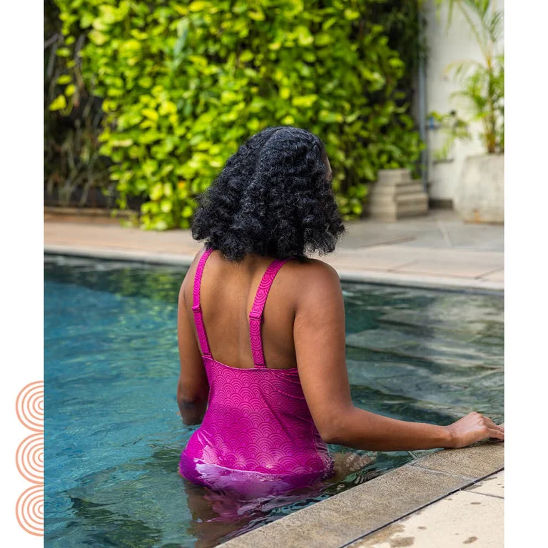A woman in a pool, her back to the camera, wearing a purple swimsuit from Gudrun Sjödén.