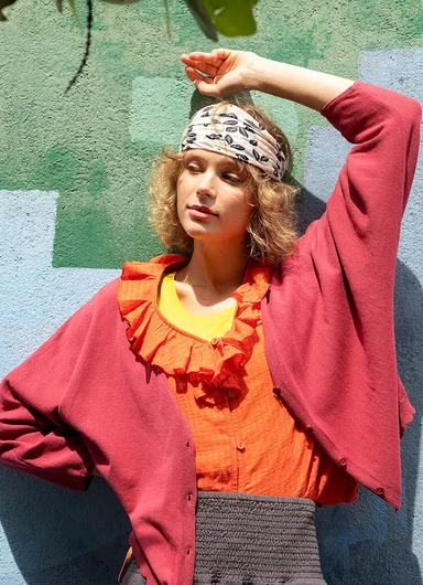 A woman leaning against a graffiti painted wall wearing layers of clothes from Gudrun Sjödén.