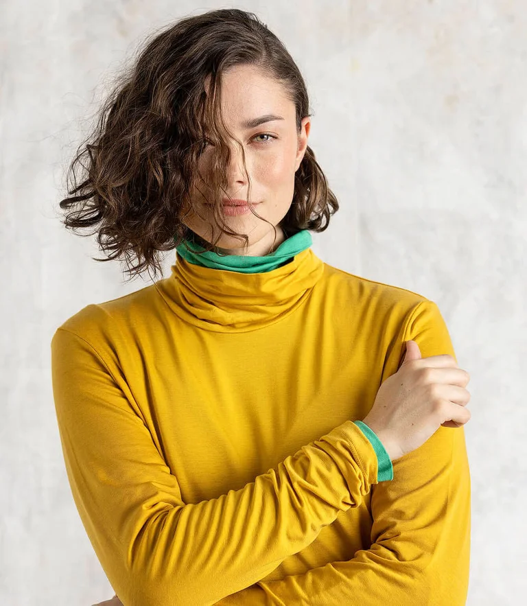 A woman wearing a yellow polo-neck top from Gudrun Sjödén.