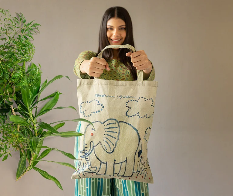 A woman holding up a tote bag featuring an elephant motif from Gudrun Sjödén.