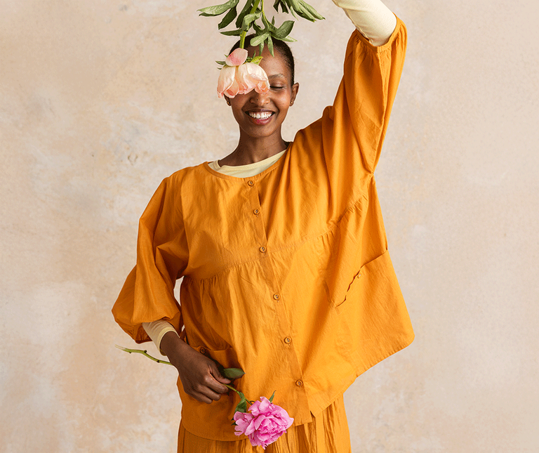 A woman holding flowers wearing orange woven essential clothes from Gudrun Sjödén.
