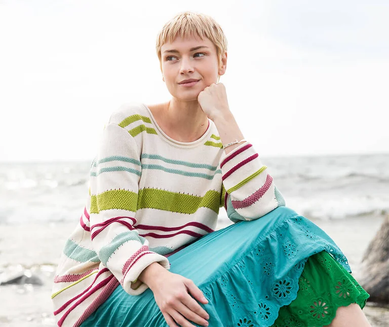 A woman wearing a striped knit sweater and blue skirt from Gudrun Sjödén.