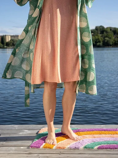 A lower body standing on a jetty with the feet on a bath mat from Gudrun Sjödén.