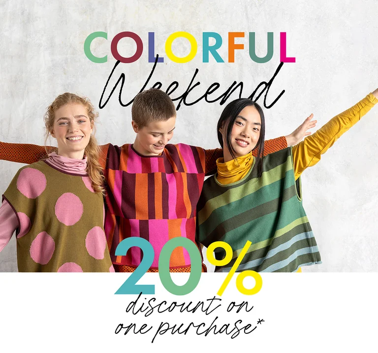 Three women standing next to one another, smiling, and holding their hands in the air, wearing colorful clothing from Gudrun Sjödén.