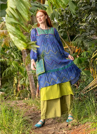 A woman wearing a pink, patterned dress and a small, pink bag adorned with mirrors from Gudrun Sjödén.