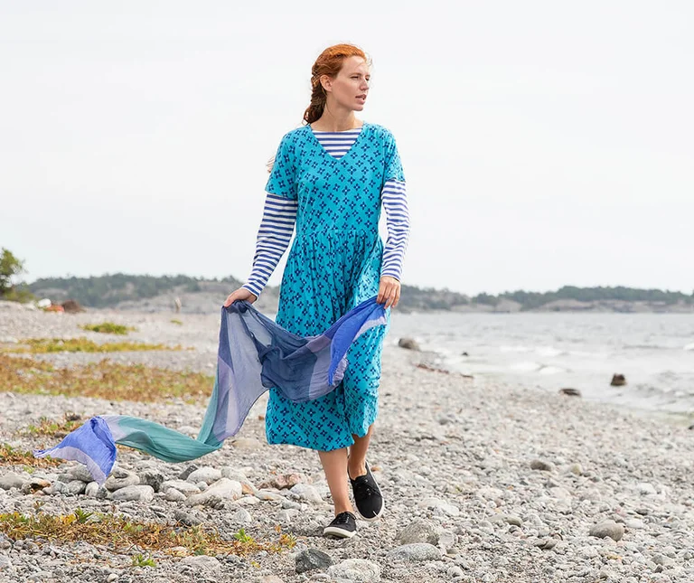 A woman wearing a patterned dress and holding a scarf from Gudrun Sjödén. 